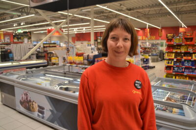 Foto viser Marte Nyberg inne på Coop Extra. I ein raud genser ser ho mot kamera og smiler.