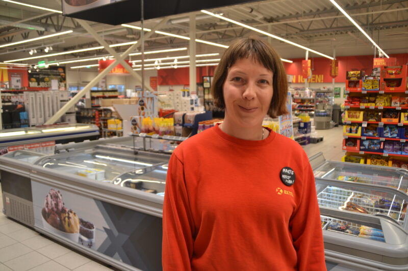 Foto viser Marte Nyberg inne på Coop Extra. I ein raud genser ser ho mot kamera og smiler.