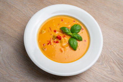 Oransj suppe ligg i eit fat, dekorert med chilli og basilikum. Kyllingsuppe med brød.