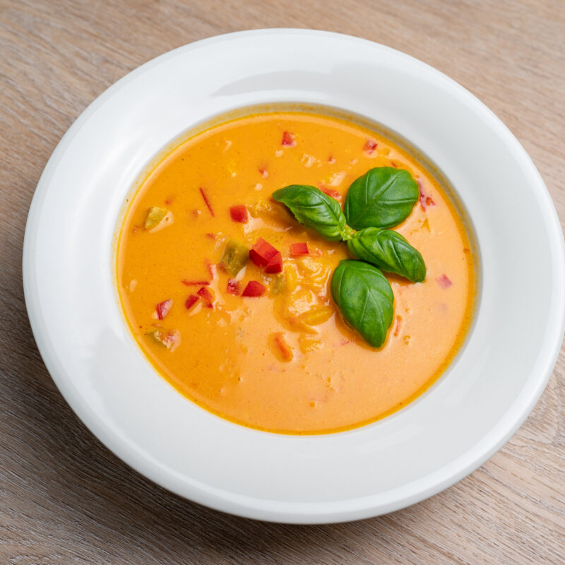 Oransj suppe ligg i eit fat, dekorert med chilli og basilikum. Kyllingsuppe med brød.