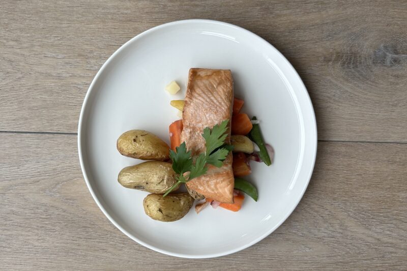 Bilete visar kvit fat med steikt laksefilet, grønsaker og steikt potet pynta med persilledusk.