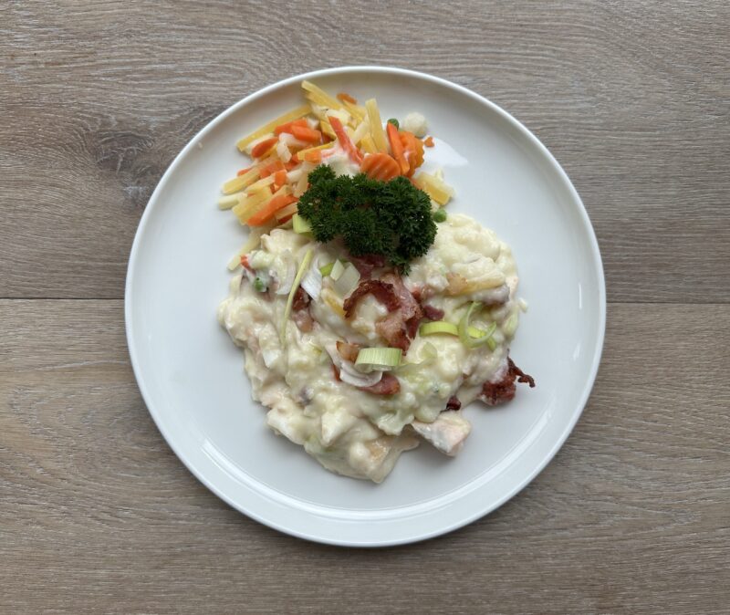 Bilete visar eit kvit fat med plukkfisk med strimla grønsaker, pyntet med persilledusk og purreløk.