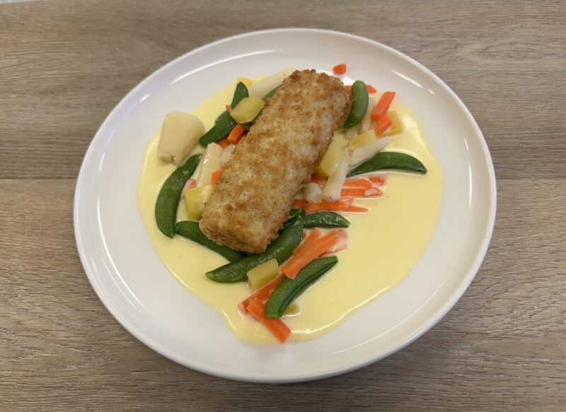 Bilete visar eit kvit fat med sprøsteikt fiskerullade, grønsaker og saus.